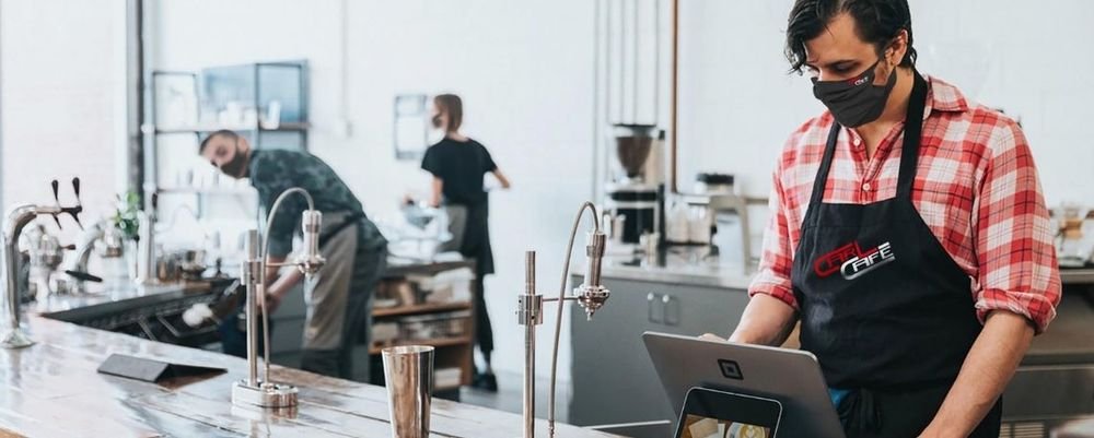Tablier noir floqué du logo « Carl Café » porté par un barista