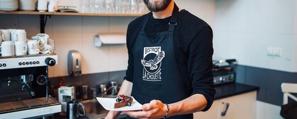 Black apron printed with the "Bistrot La Chouette" logo worn by a waiter