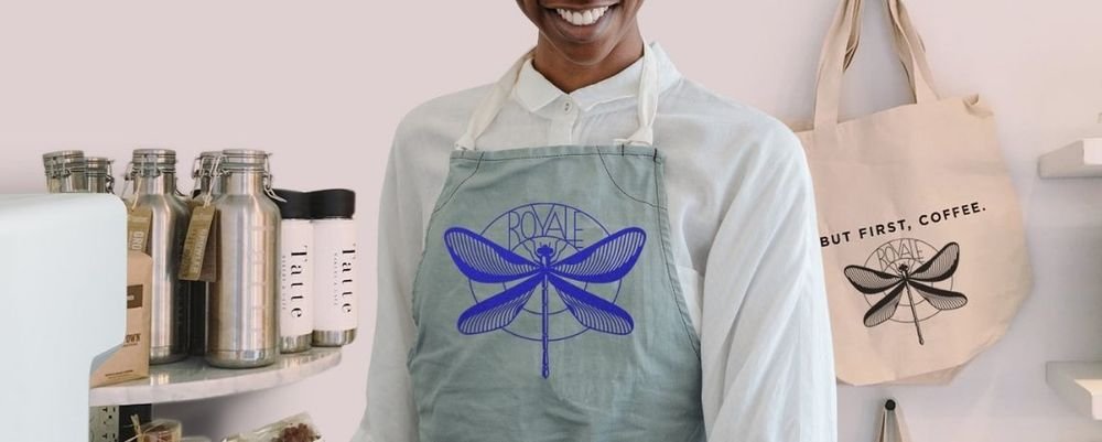 Grey apron printed with a blue dragonfly, Royale logo, with matching tote bag