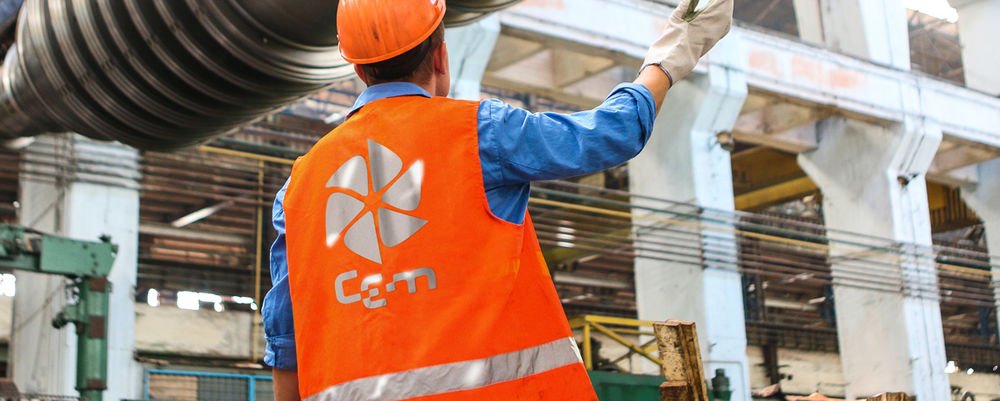 Orange workwear printed with the "Cem" logo in an industrial workshop